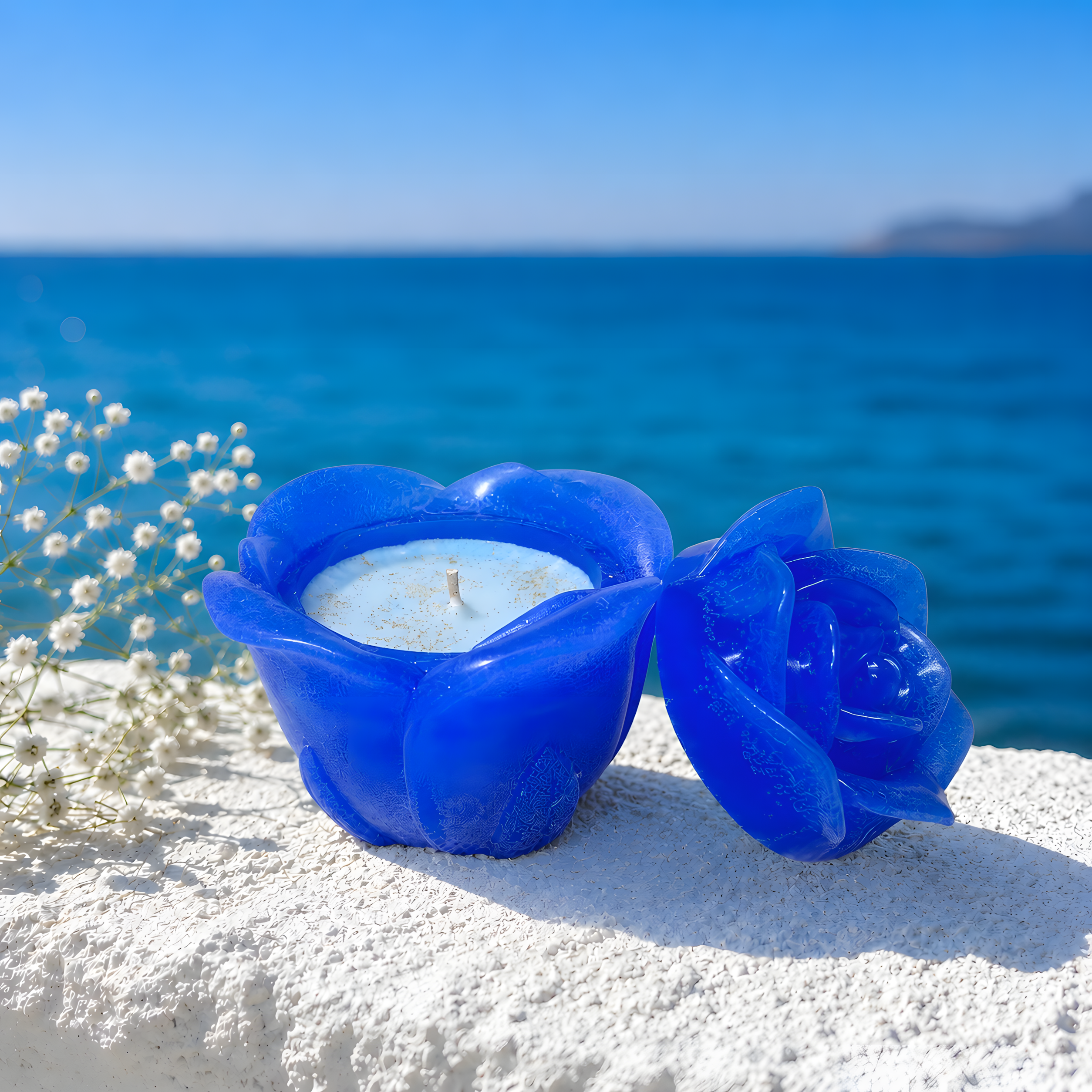 Blue flower-shaped candle holder with a white candle on a sandy surface with ocean in the background