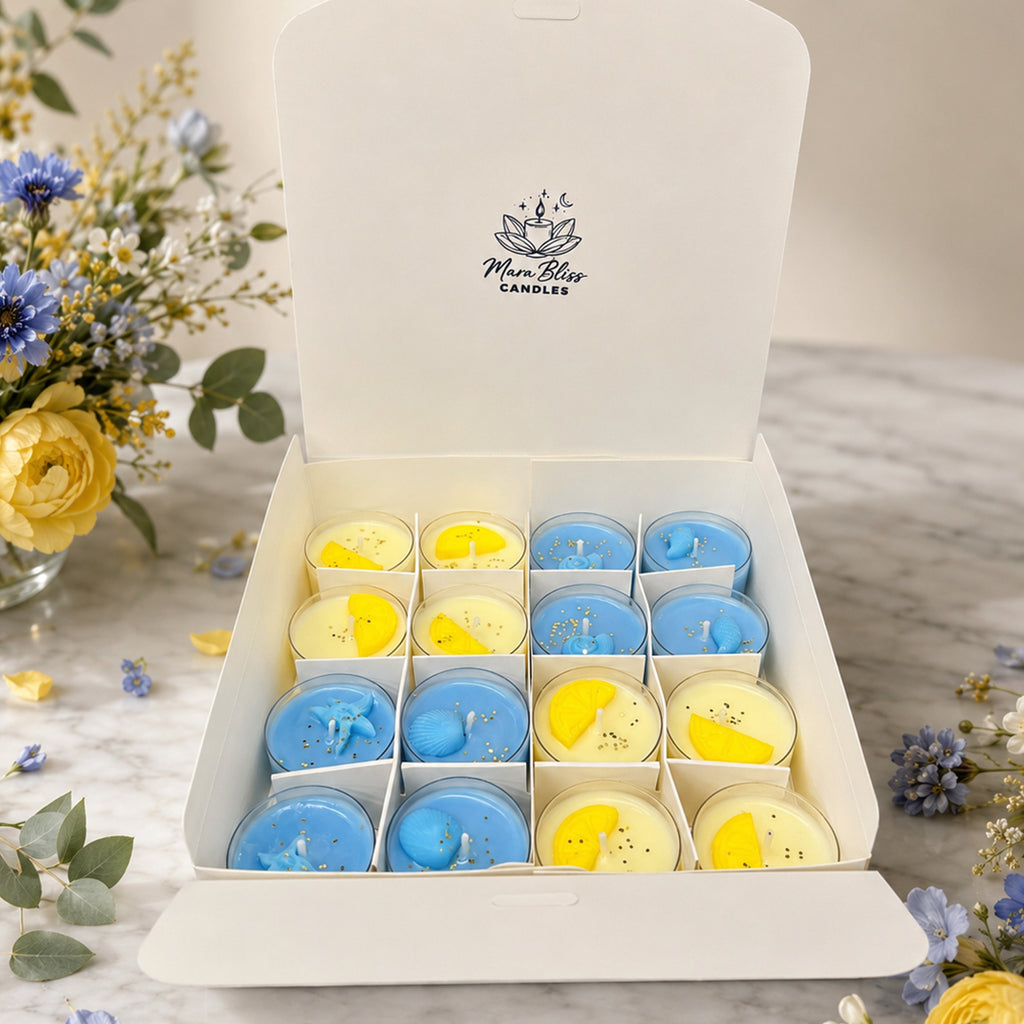 Box of small candles in blue and yellow with Man Bliss Candles logo, surrounded by flowers on a marble surface.