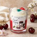A cherry-themed scented candle in a clear glass jar, styled with whipped cream, a red cherry, and a green wax accent on top. The label reads 'Sweet Cherry' and 'Handgjort Ljus I Sojavay'.