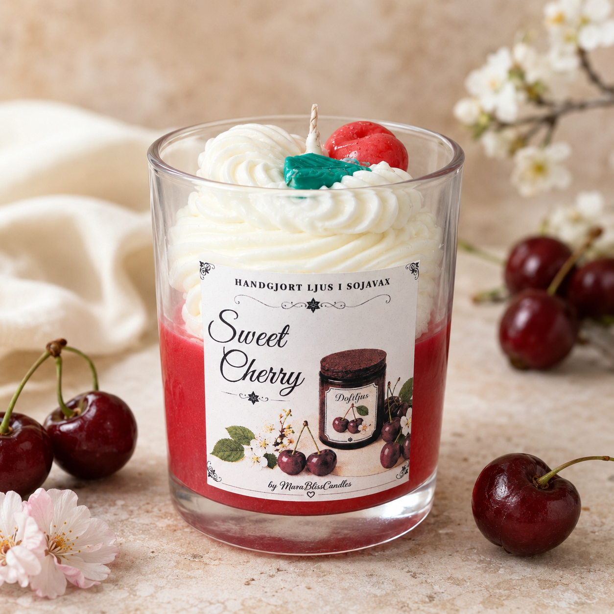 A cherry-themed scented candle in a clear glass jar, styled with whipped cream, a red cherry, and a green wax accent on top. The label reads 'Sweet Cherry' and 'Handgjort Ljus I Sojavay'.