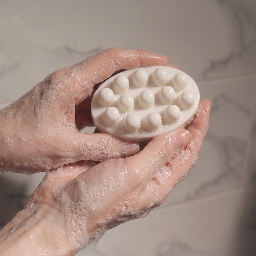 Hand holding a white scrubber with a textured surface against a neutral background